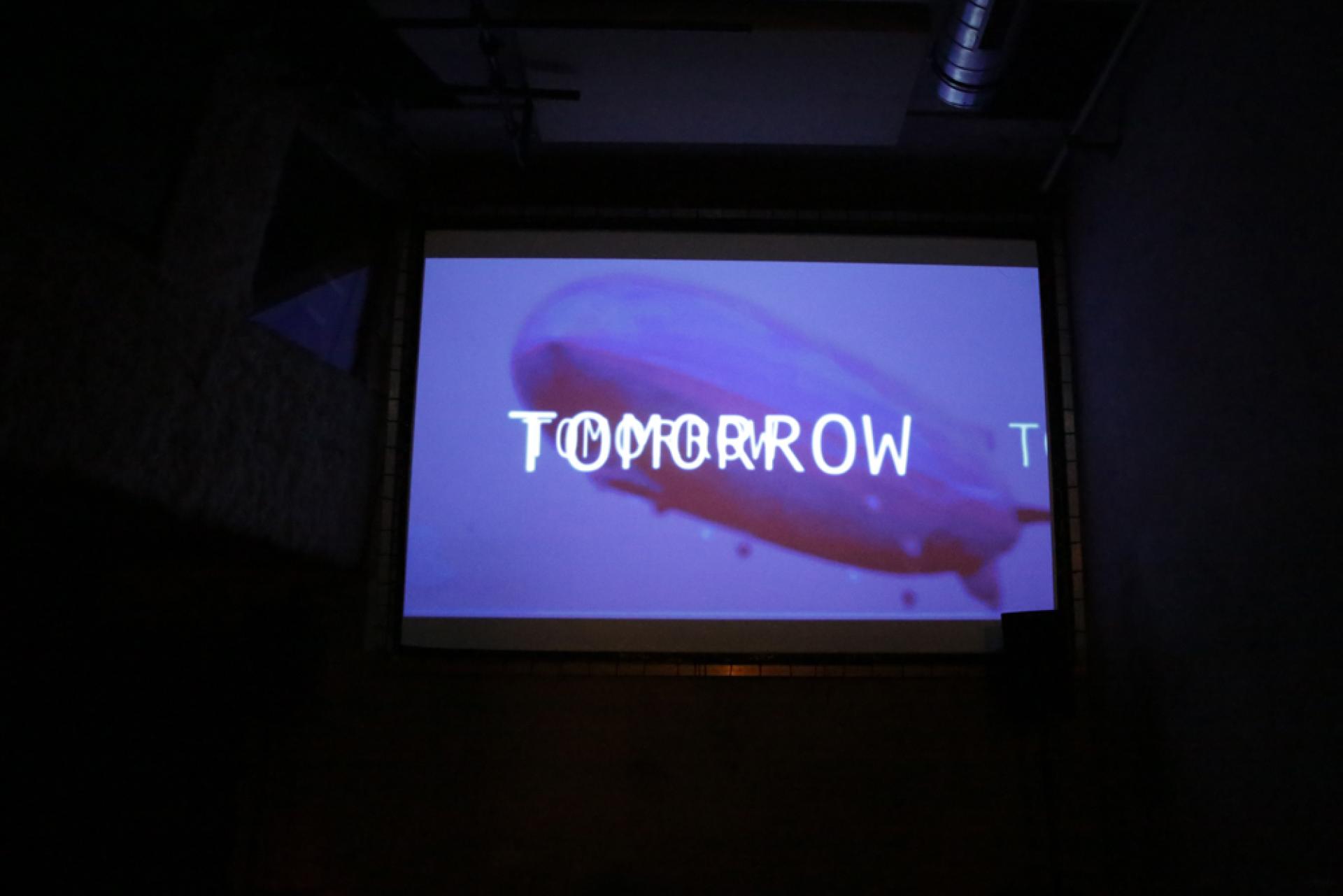 Foto der Videoinstallation von lowers, zu sehen ist ein Zeppelin auf dem "Tomorrow" steht