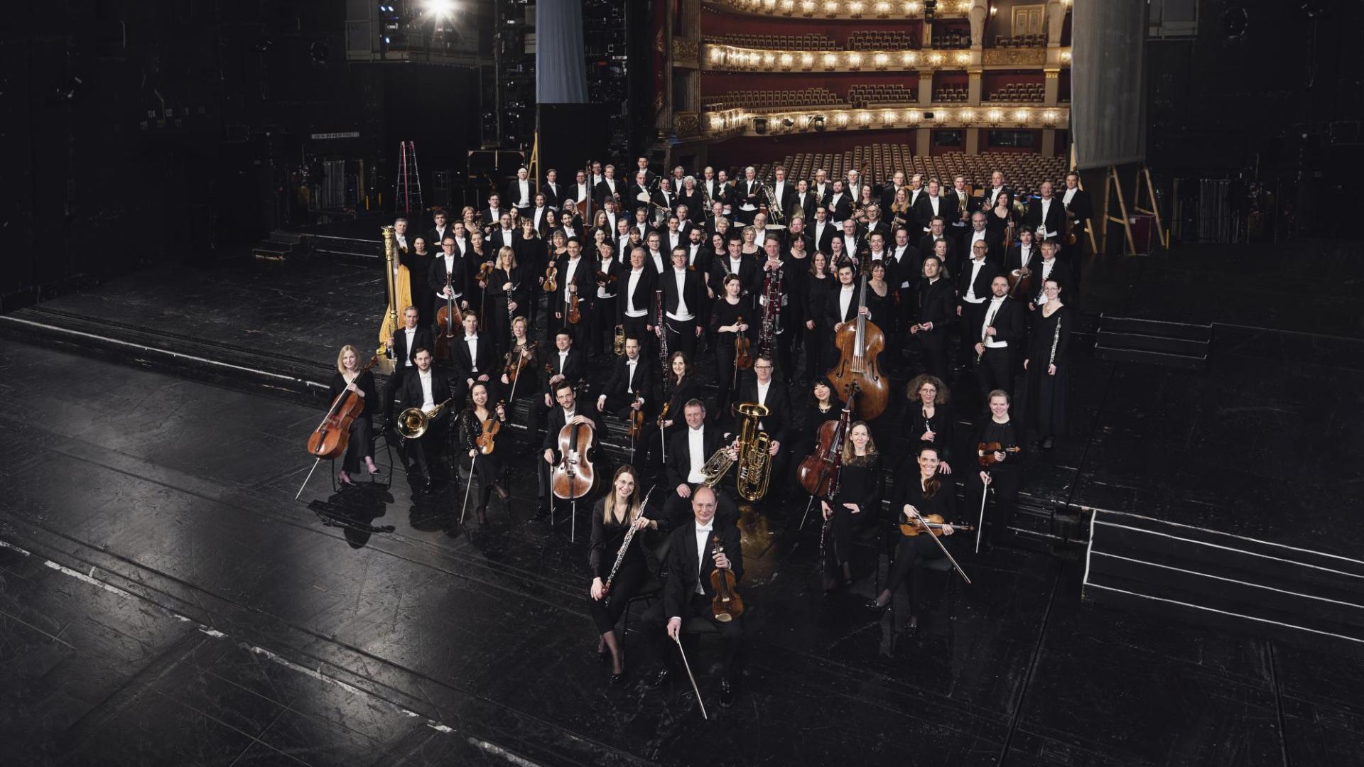 The orchestra is gathered on stage with its instruments.