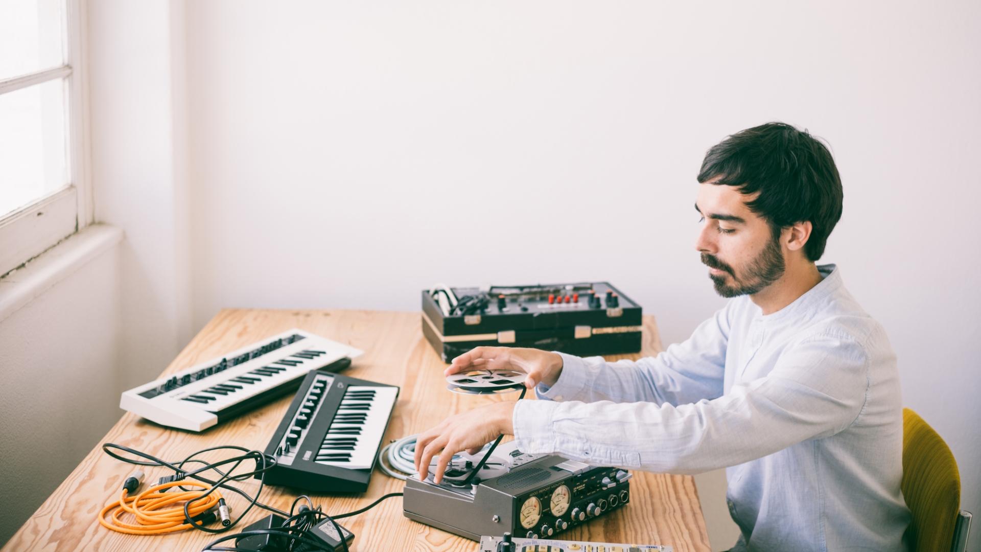 Mann im weißen Hemd sitzt an einem Schreibtisch mit Musikanlage